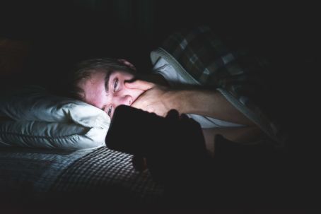Mann mit Smartphone nachts im Bett